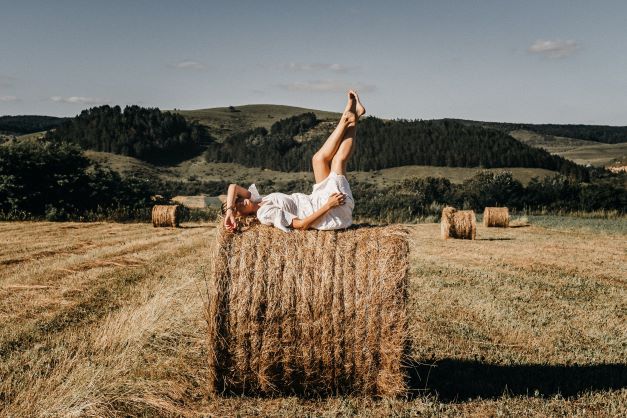 žena leží na seně přes letní den v přírodě a v bílých šatech